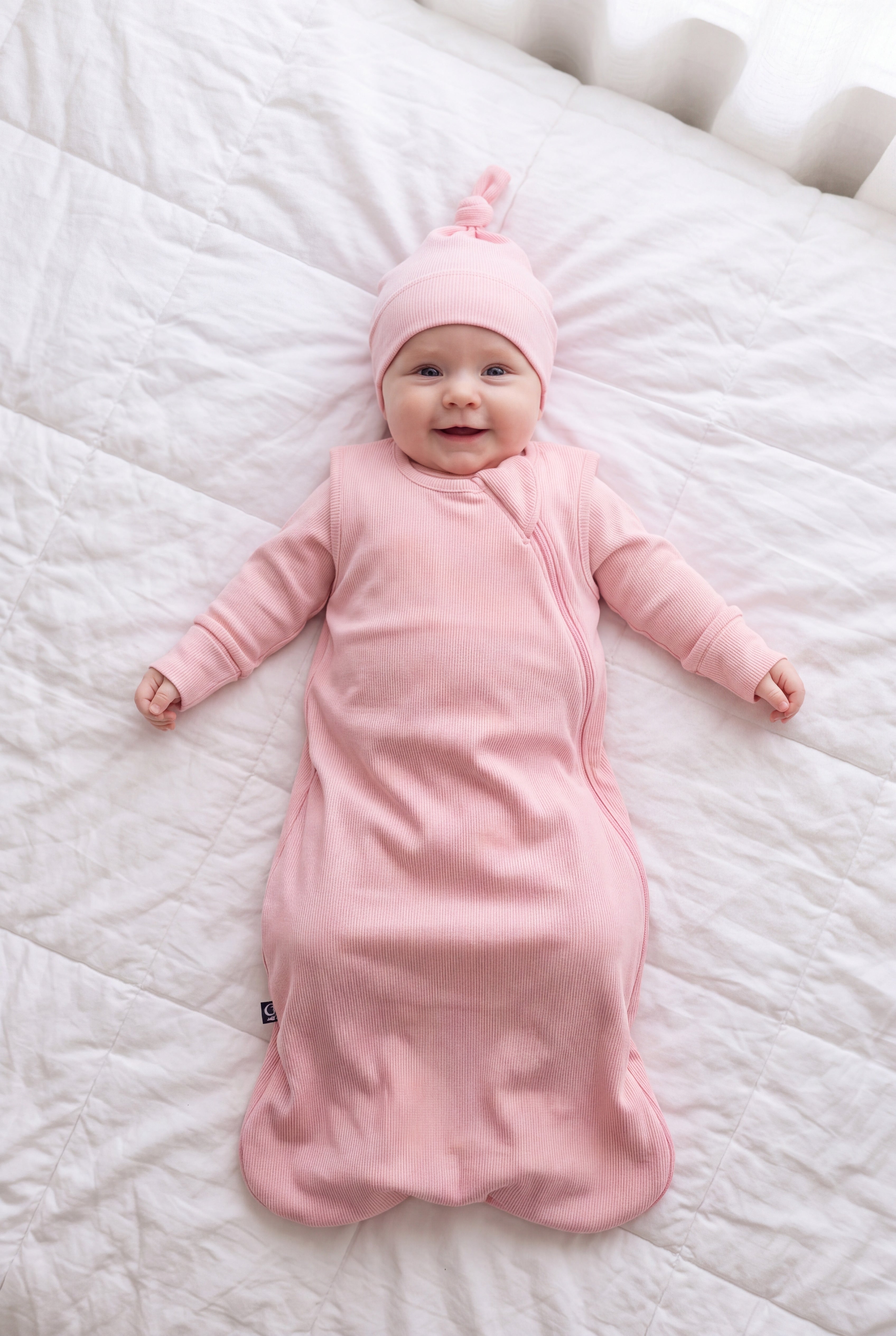 Baby in the Hugs & Giggles bamboo sleep bag in Blush with matching romper and knotted hat, top-down view