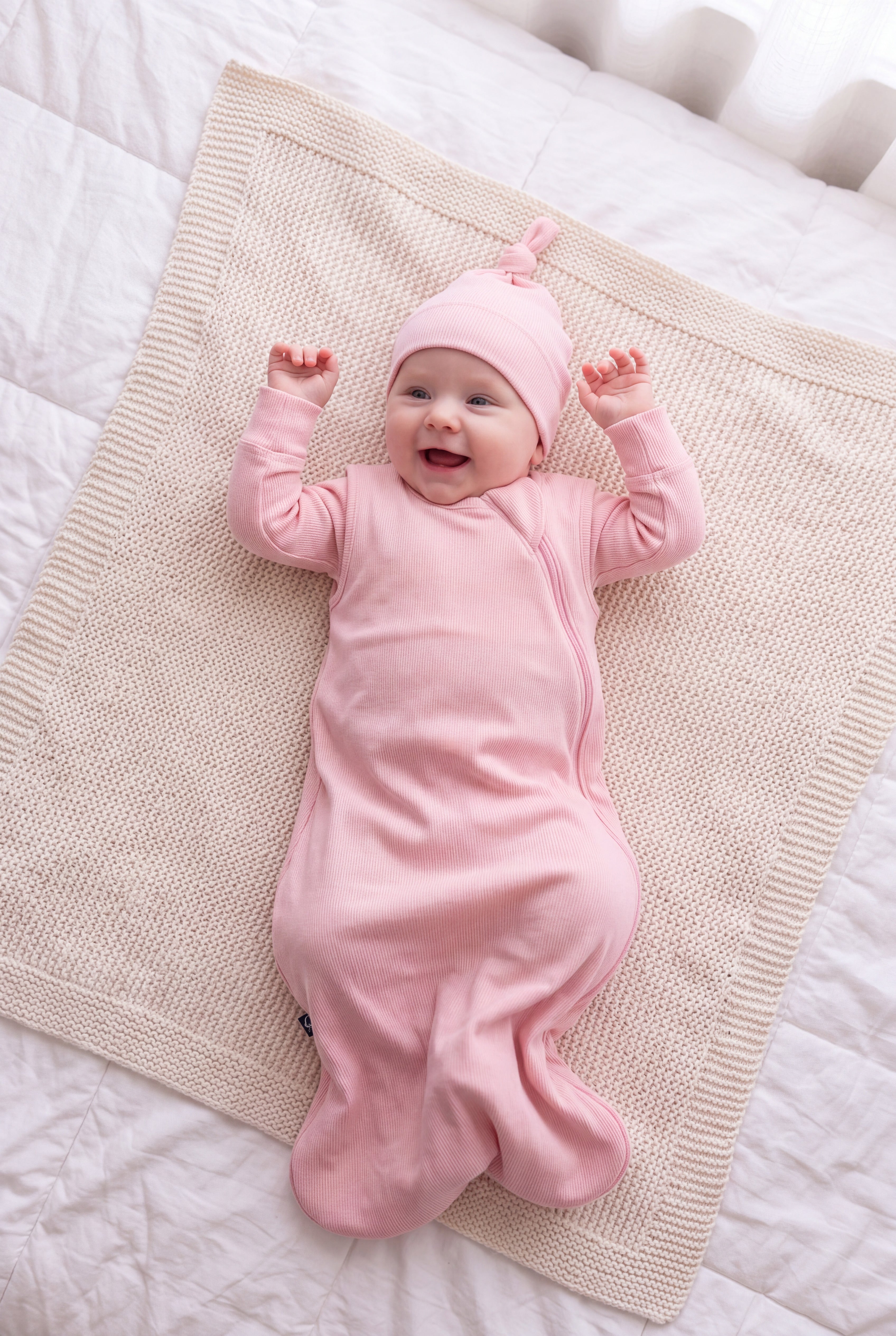 Laughing baby in the Blush bamboo sleep bag and matching hat on a knit blanket
