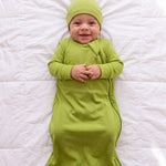 Baby in the Hugs & Giggles bamboo sleep bag in Olly green with matching romper and knotted hat, top-down view