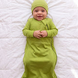 Baby in the Hugs & Giggles bamboo sleep bag in Olly green with matching romper and knotted hat, top-down view