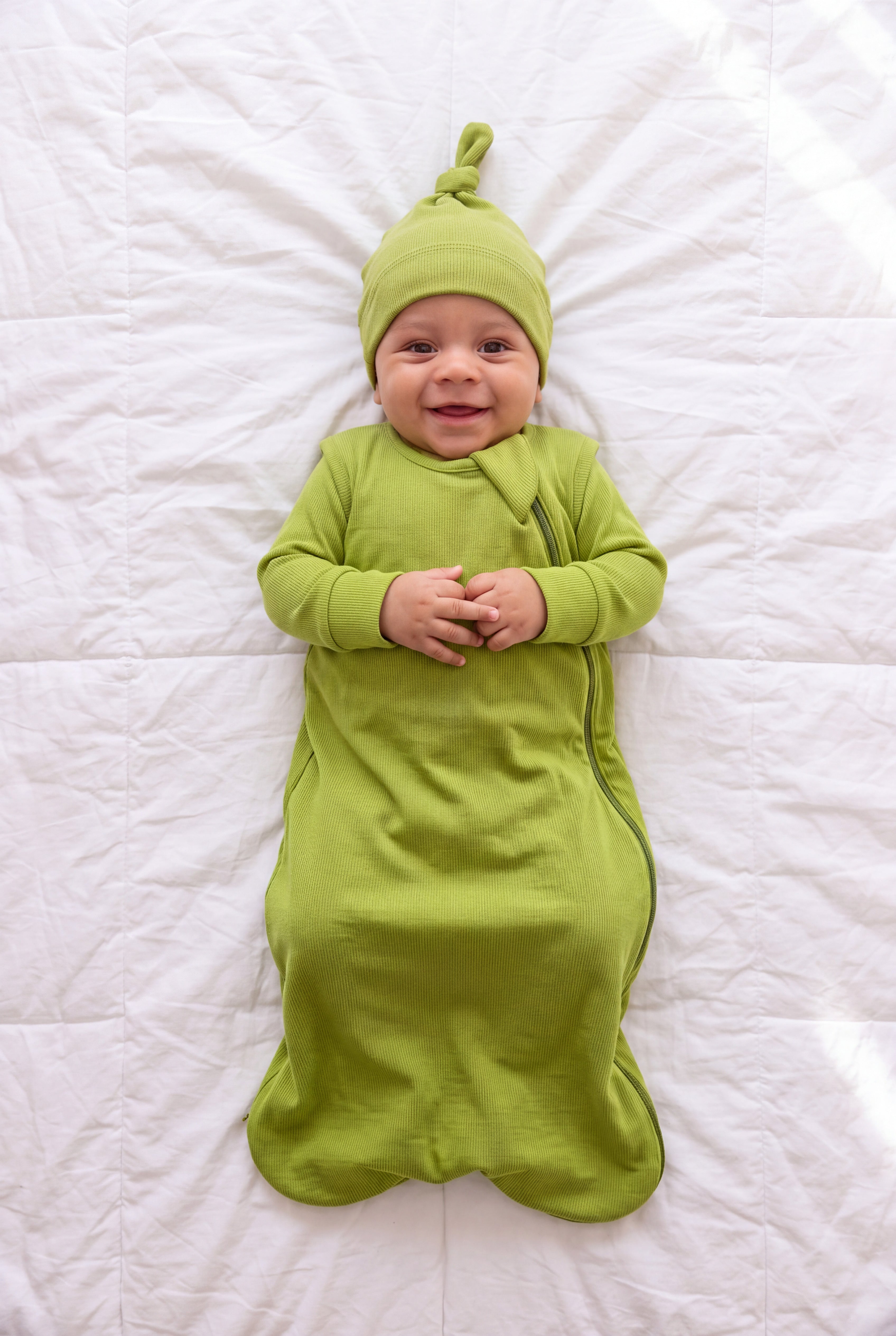 Baby in the Hugs & Giggles bamboo sleep bag in Olly green with matching romper and knotted hat, top-down view