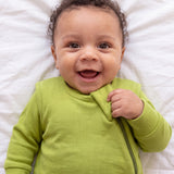 Close-up of a giggling baby holding the zipper flap of the Olly green ribbed bamboo sleep bag