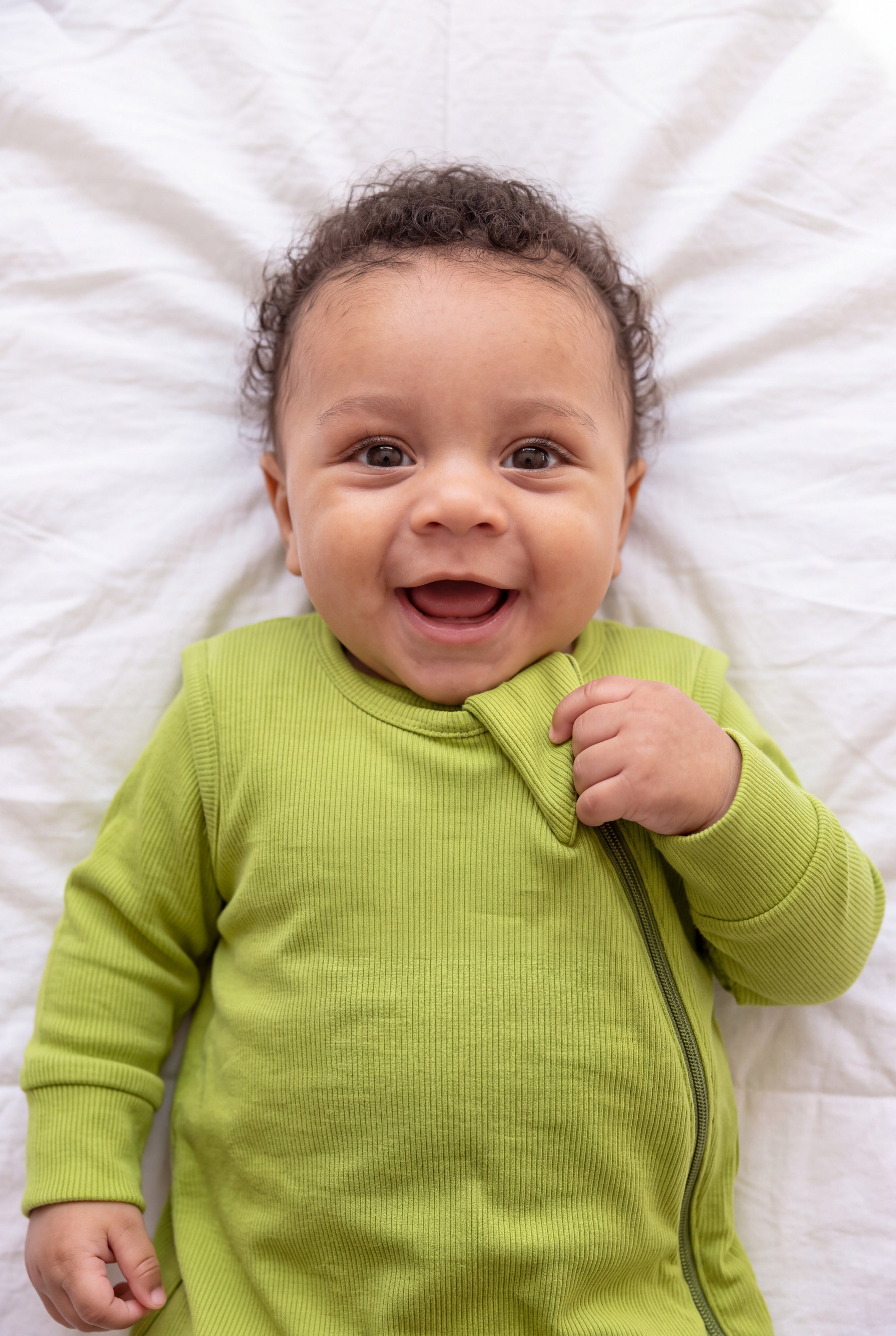 Close-up of a giggling baby holding the zipper flap of the Olly green ribbed bamboo sleep bag