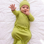 Baby reaching toward the camera in the Olly green bamboo sleep bag and matching hat
