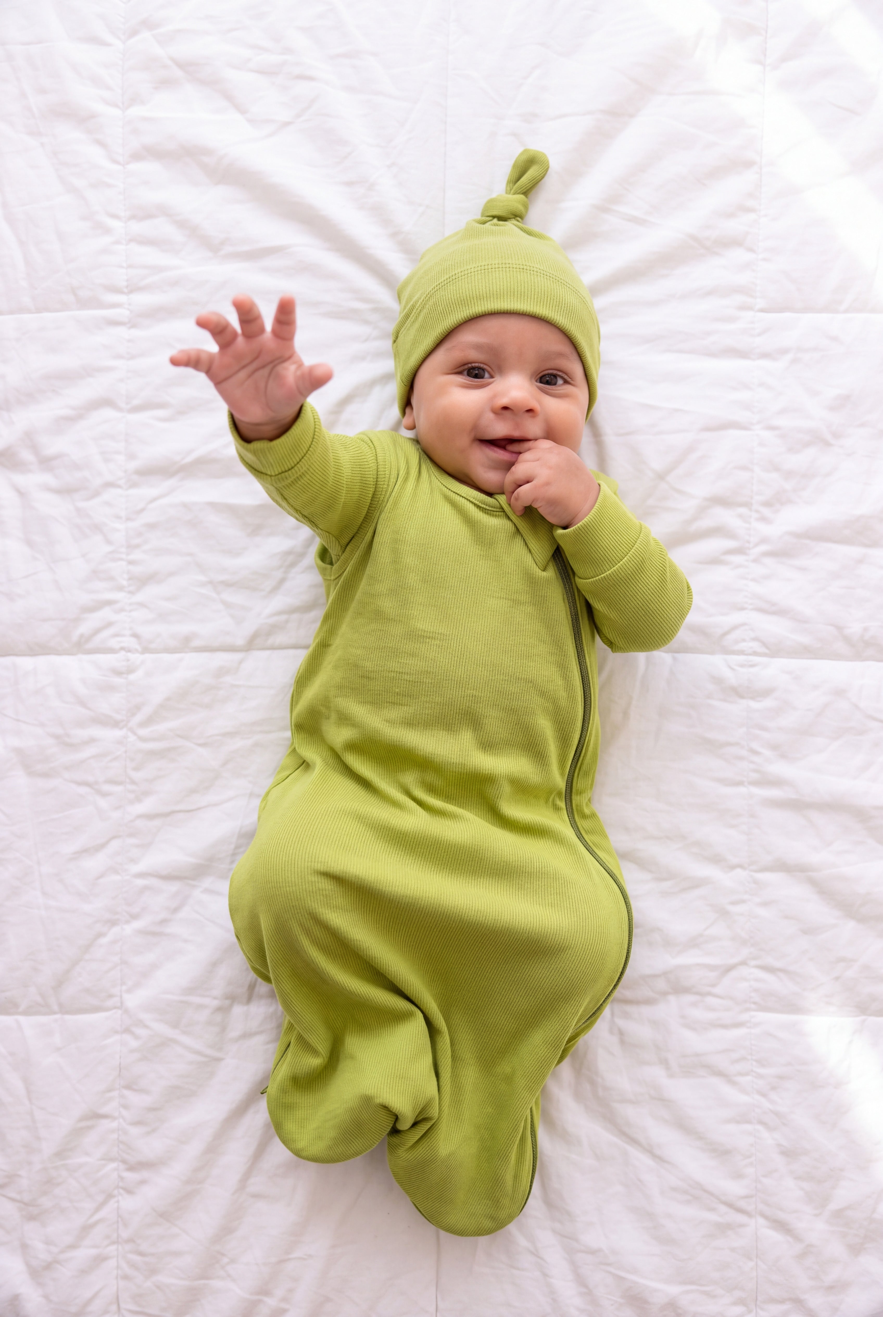 Baby reaching toward the camera in the Olly green bamboo sleep bag and matching hat